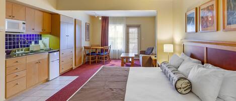A hotel room with a bed, a desk, a chair, a microwave, a refrigerator, and a window with curtains.