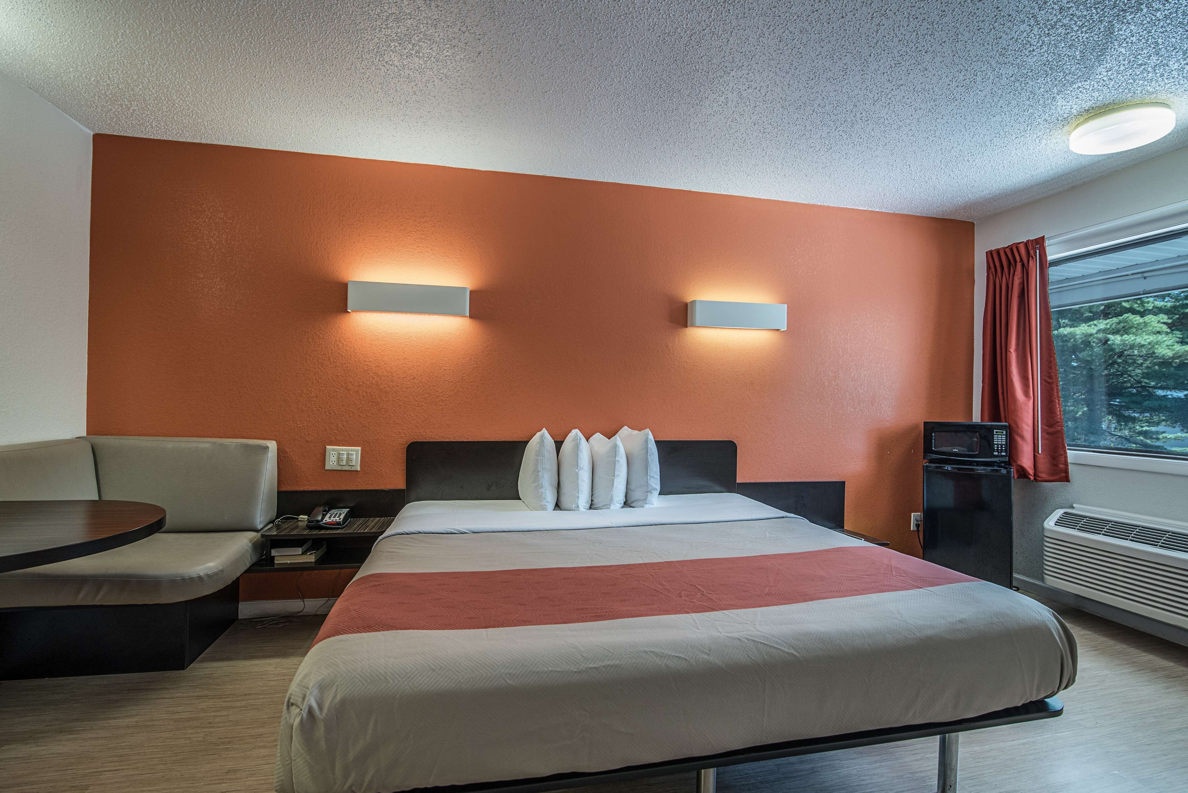 Habitación de hotel con cama, escritorio, silla, microondas y ventana con cortinas.