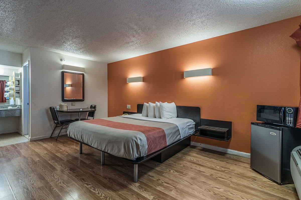 A modern hotel room with a bed, a desk, a chair, a small refrigerator, and a microwave.