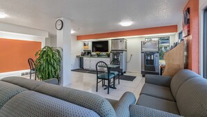 Una sala de estar moderna con un conjunto de sofá, un comedor con mesa y sillas, y una cocina equipada con electrodomésticos y un refrigerador.
