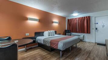 A hotel room with a bed, a desk, a chair, a TV, and a wardrobe.