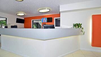 Un espace d’accueil avec un comptoir blanc, des murs d’accent orange et une plante sur le côté droit.