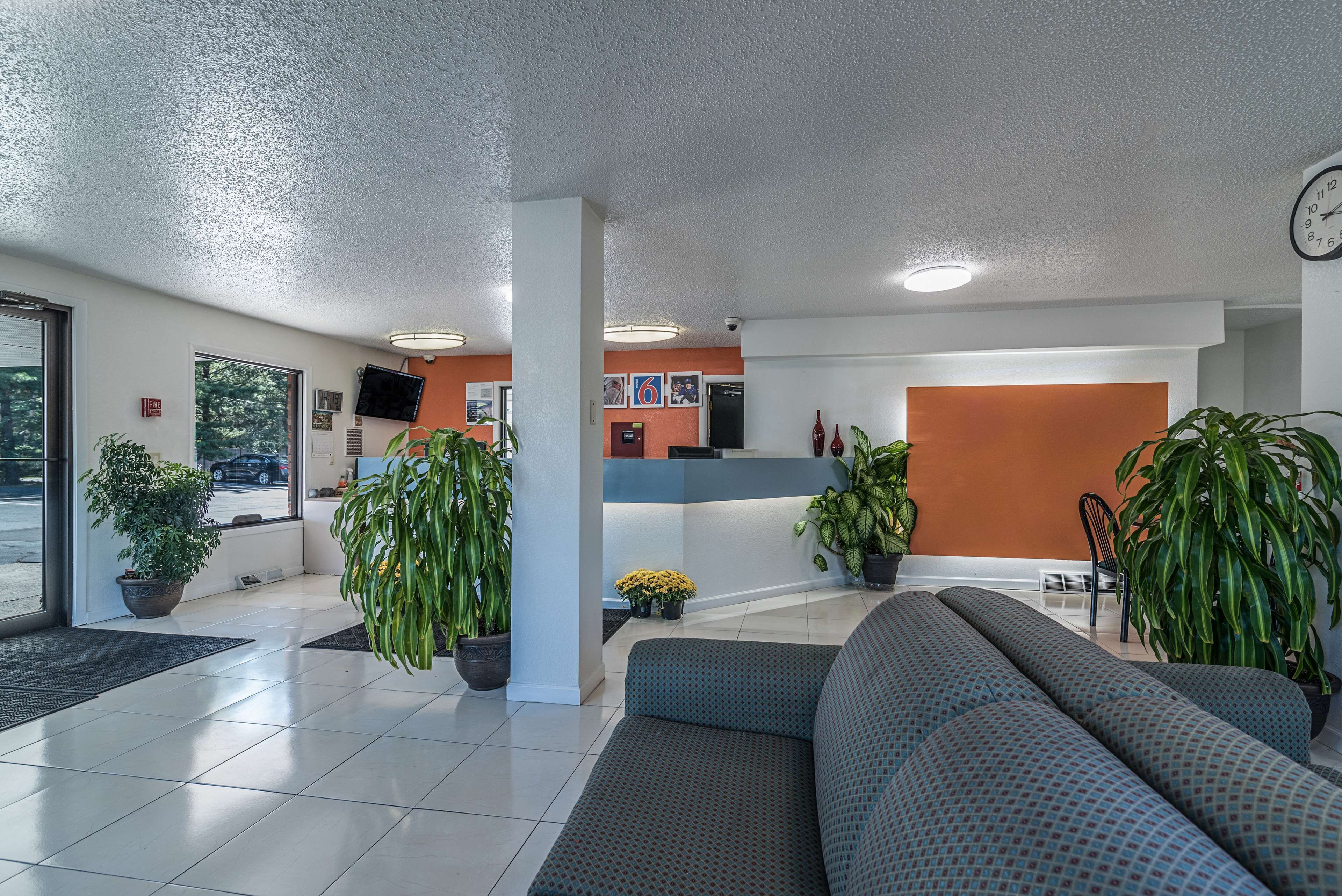 A lobby with a reception desk, seating area, potted plants, and a clock on the wall.