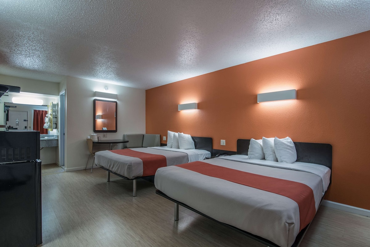 A hotel room with two beds, a desk, a chair, and a television.