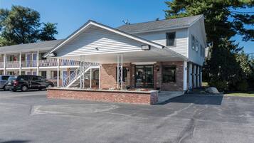 A motel with a covered front porch, brick foundation, and a staircase leading to the entrance.