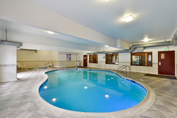 An indoor swimming pool with clear blue water, tiled floor, and a pool ladder.