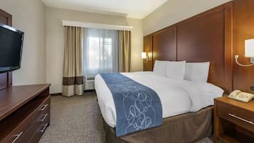 A hotel room with a large bed, a television, a desk, and a window with curtains.