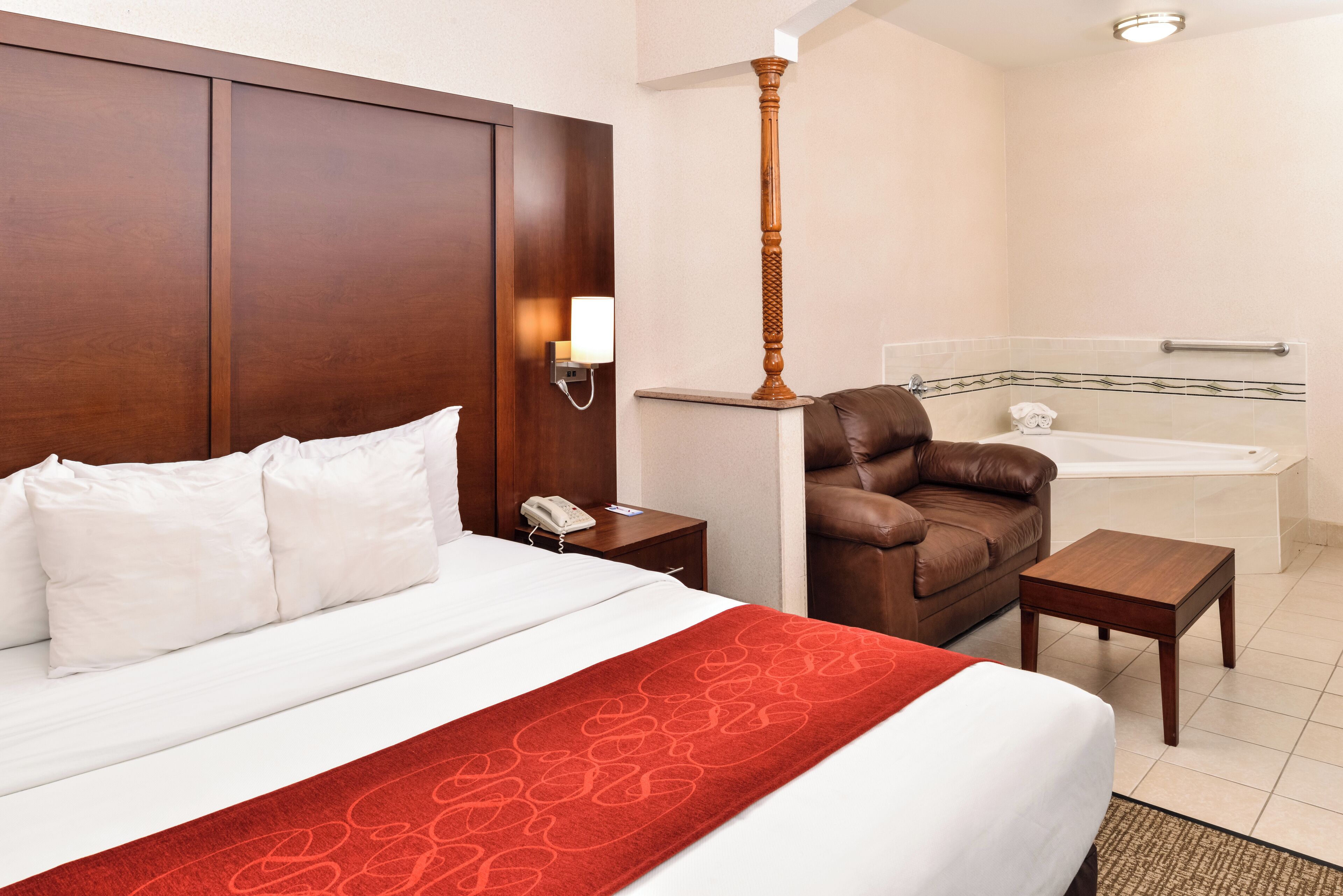 Ein Hotelzimmer mit einem großen Bett, einem Ledersessel, einem kleinen Tisch, einem Nachttisch und einem Badezimmer mit einer Badewanne.