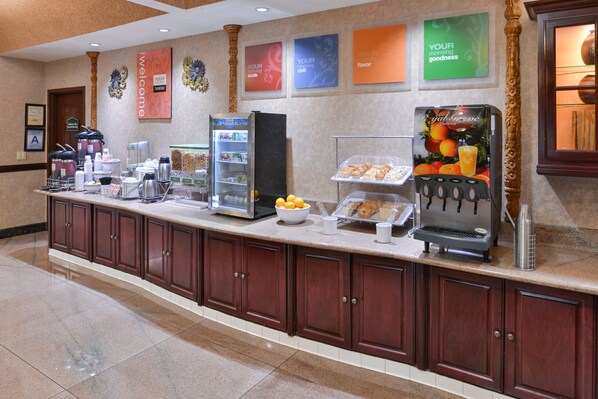 A hotel breakfast area with a self-serve station, refrigerated display cases, and a coffee machine. - Citrus Suites Redlands Loma Linda Hotel (Redlands)