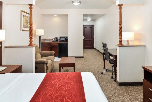 A hotel room with a bed, a desk, a chair, a sofa, a coffee machine, and a door leading to a bathroom. - Citrus Suites Redlands Loma Linda Hotel (Redlands)