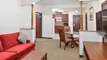 A compact living area with a red sofa, wooden dining table, and chairs, leading to a kitchenette with cabinets and a microwave.