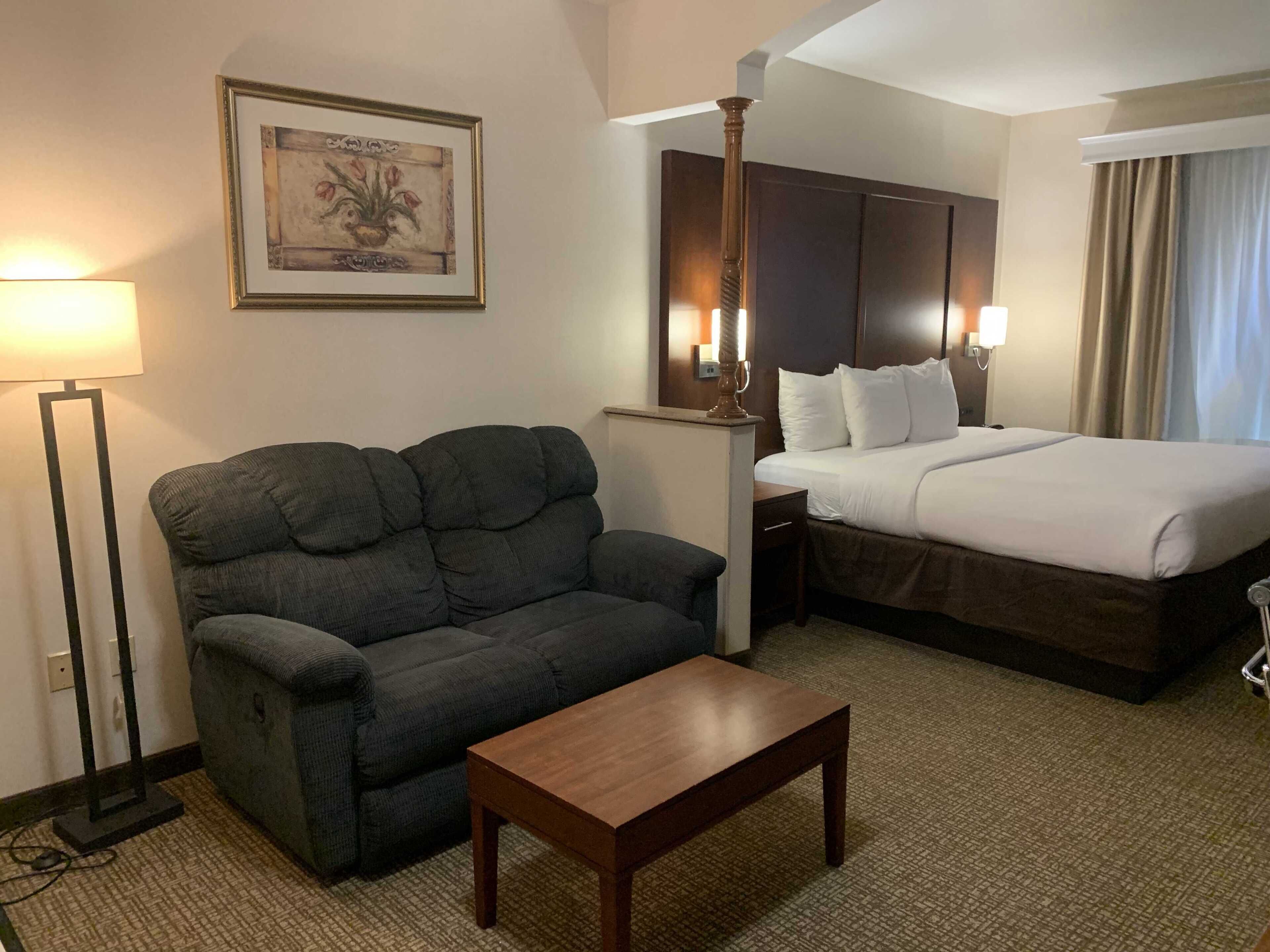 A hotel room with a sofa, a wooden table, a bed, and a framed picture on the wall.