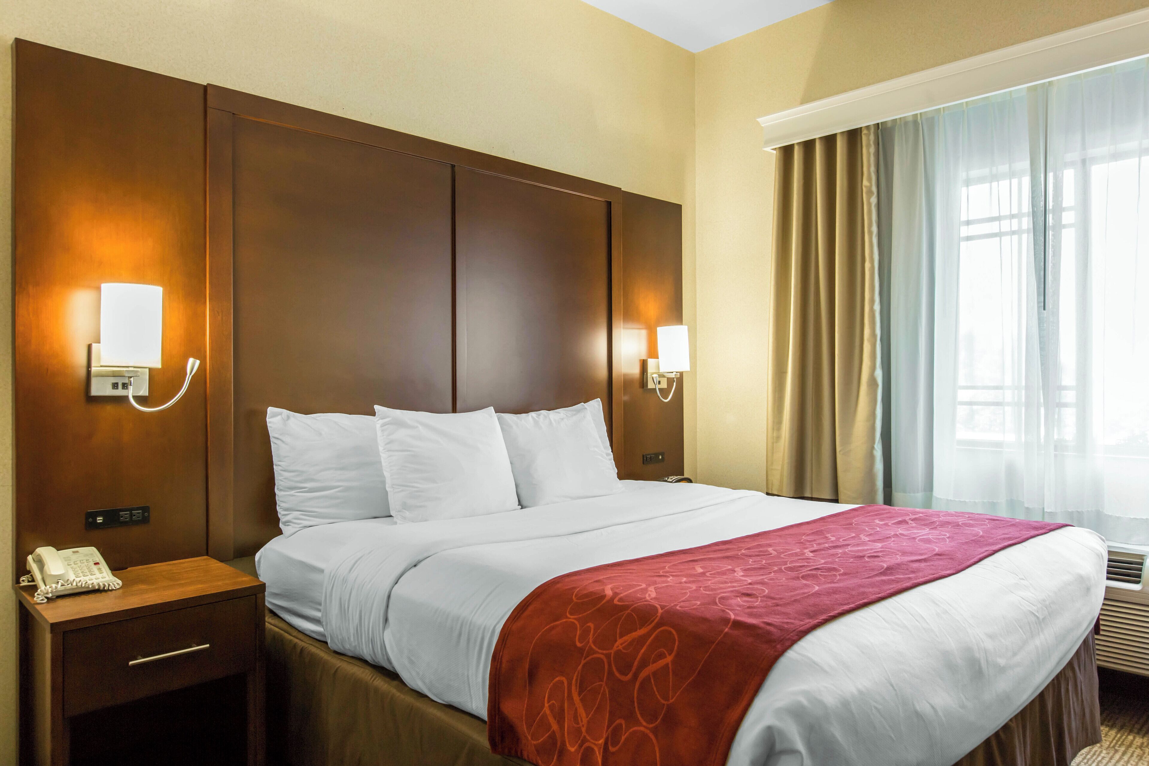 Una habitación de hotel con una cama grande, dos mesitas de noche, un teléfono y lámparas de pared.