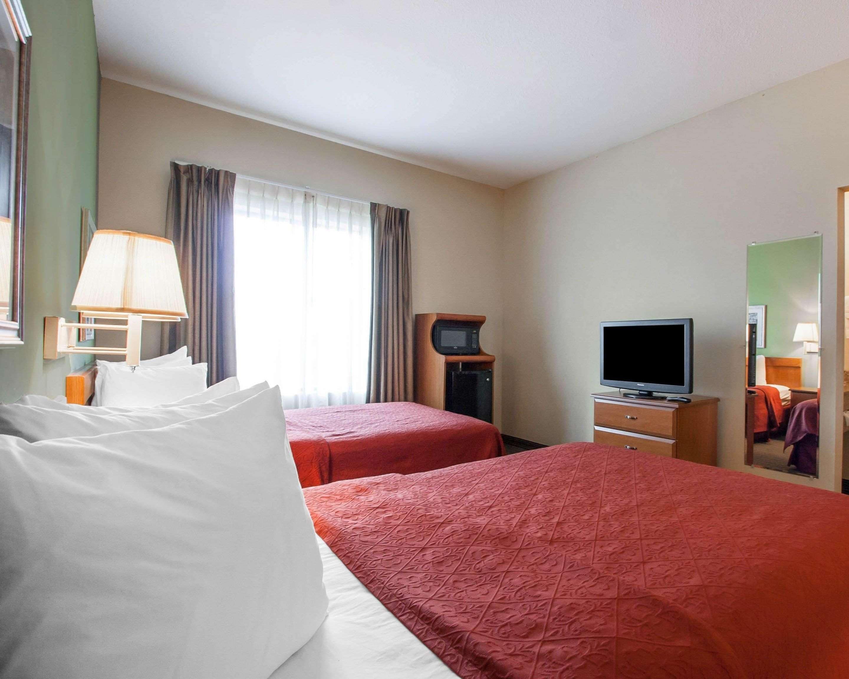 A hotel room with two beds, a television, a desk, and a window with curtains.