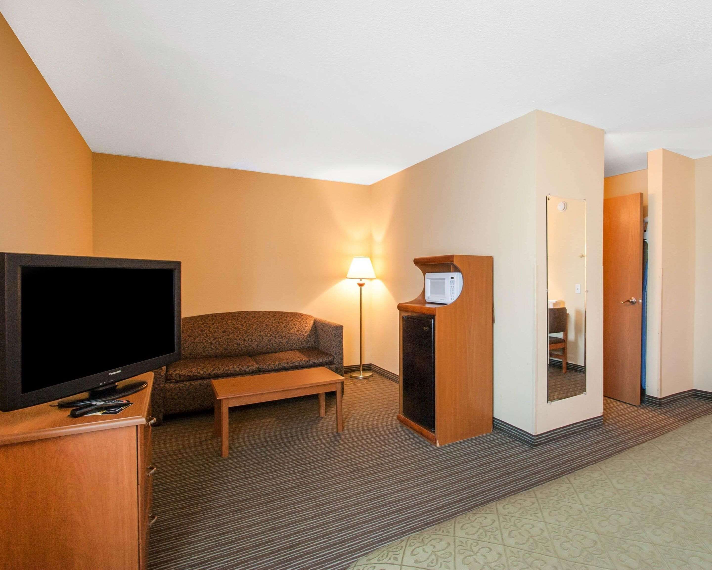 A hotel room with a flat-screen TV, a sofa, a small table, a lamp, a microwave, and a door leading to another room.