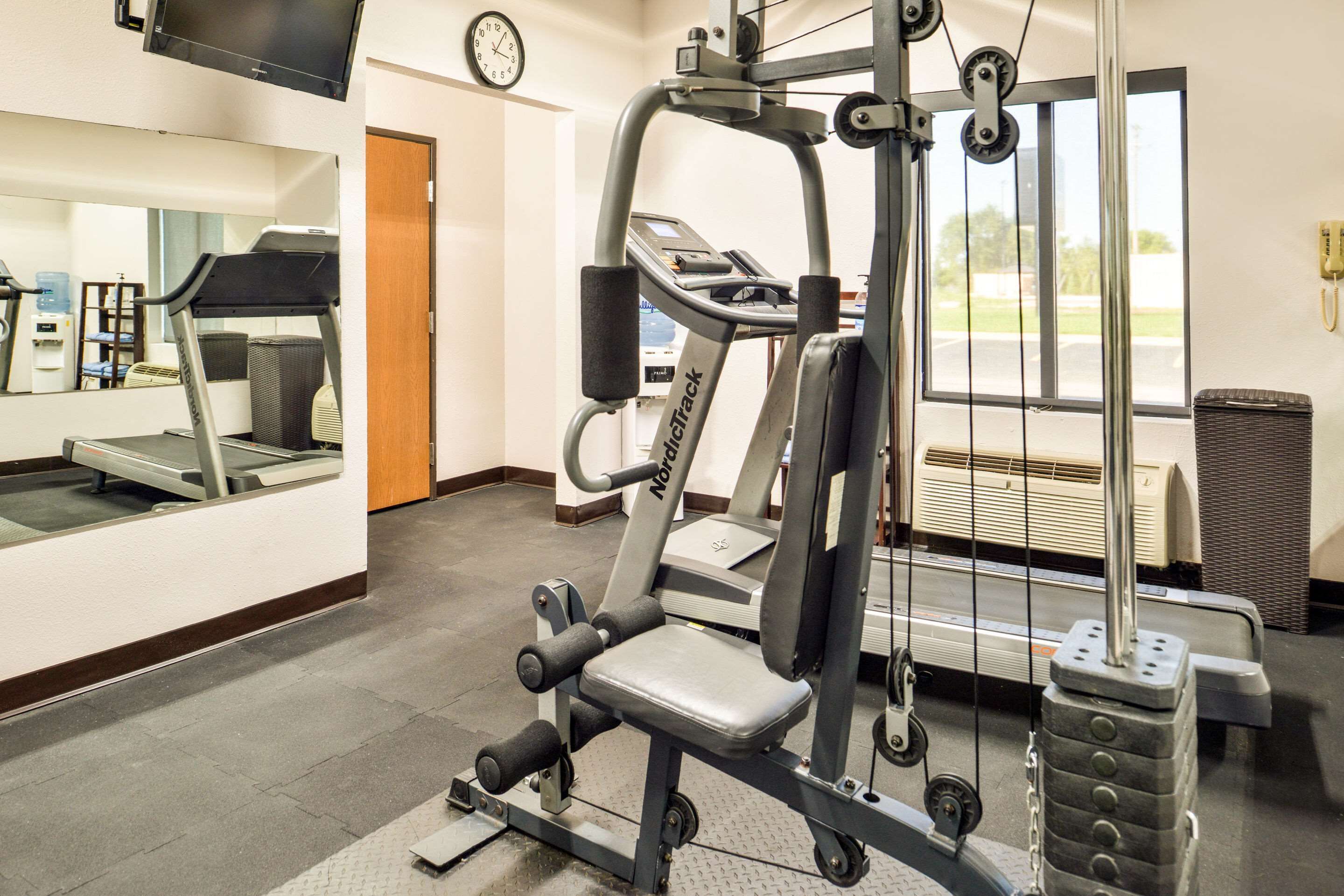 Une salle de sport équipée d’un tapis de course, de machines de musculation et d’une grande fenêtre.
