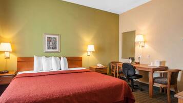 A hotel room with a large bed, a desk, two chairs, a desk lamp, a phone, and a framed picture on the wall.