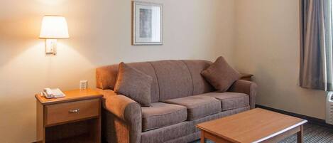 A hotel room with a sofa, a small wooden table, a nightstand with a lamp, and a framed picture on the wall.
