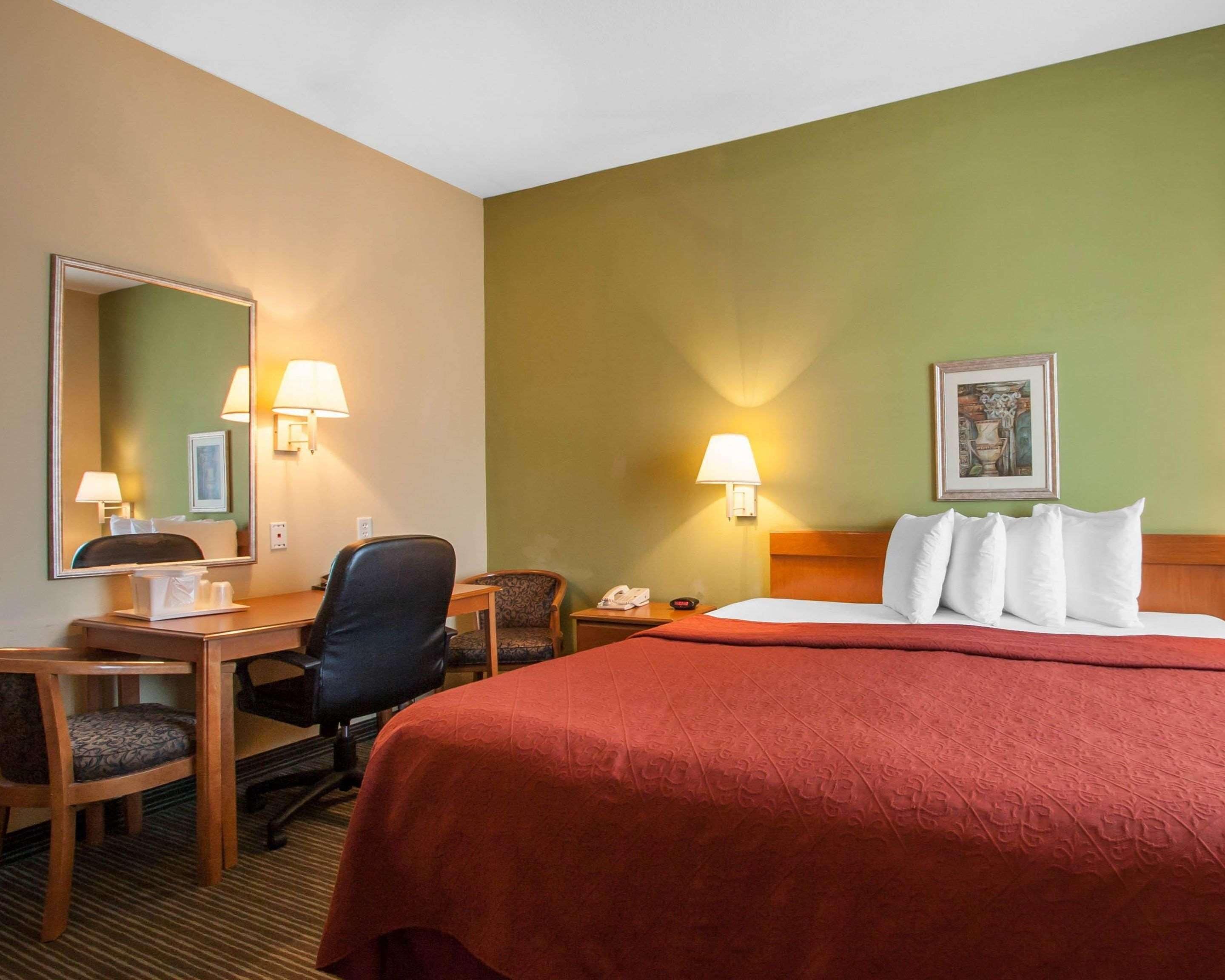 A hotel room with a bed, a desk, a chair, a telephone, and a mirror.