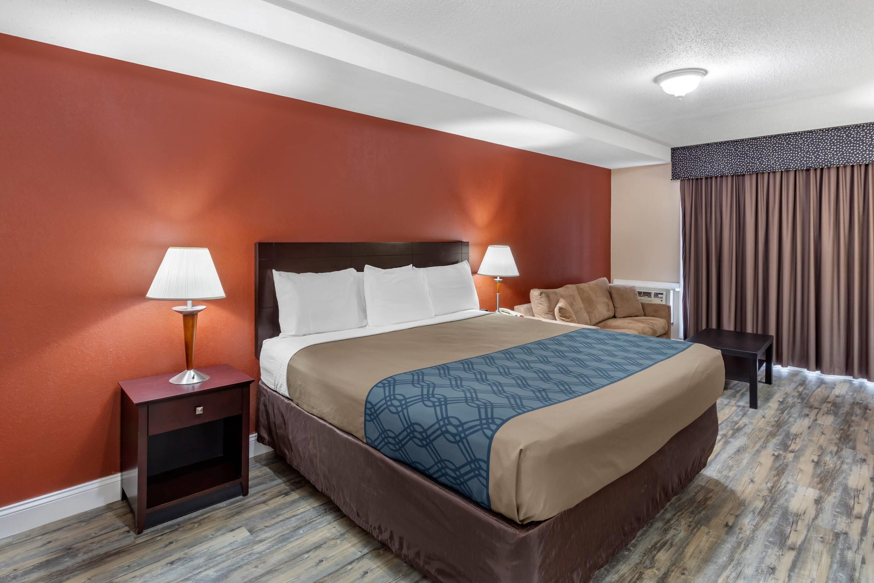 Una habitación de hotel con una cama grande, dos mesitas de noche con lámparas, un cabecero marrón y suelo de madera.