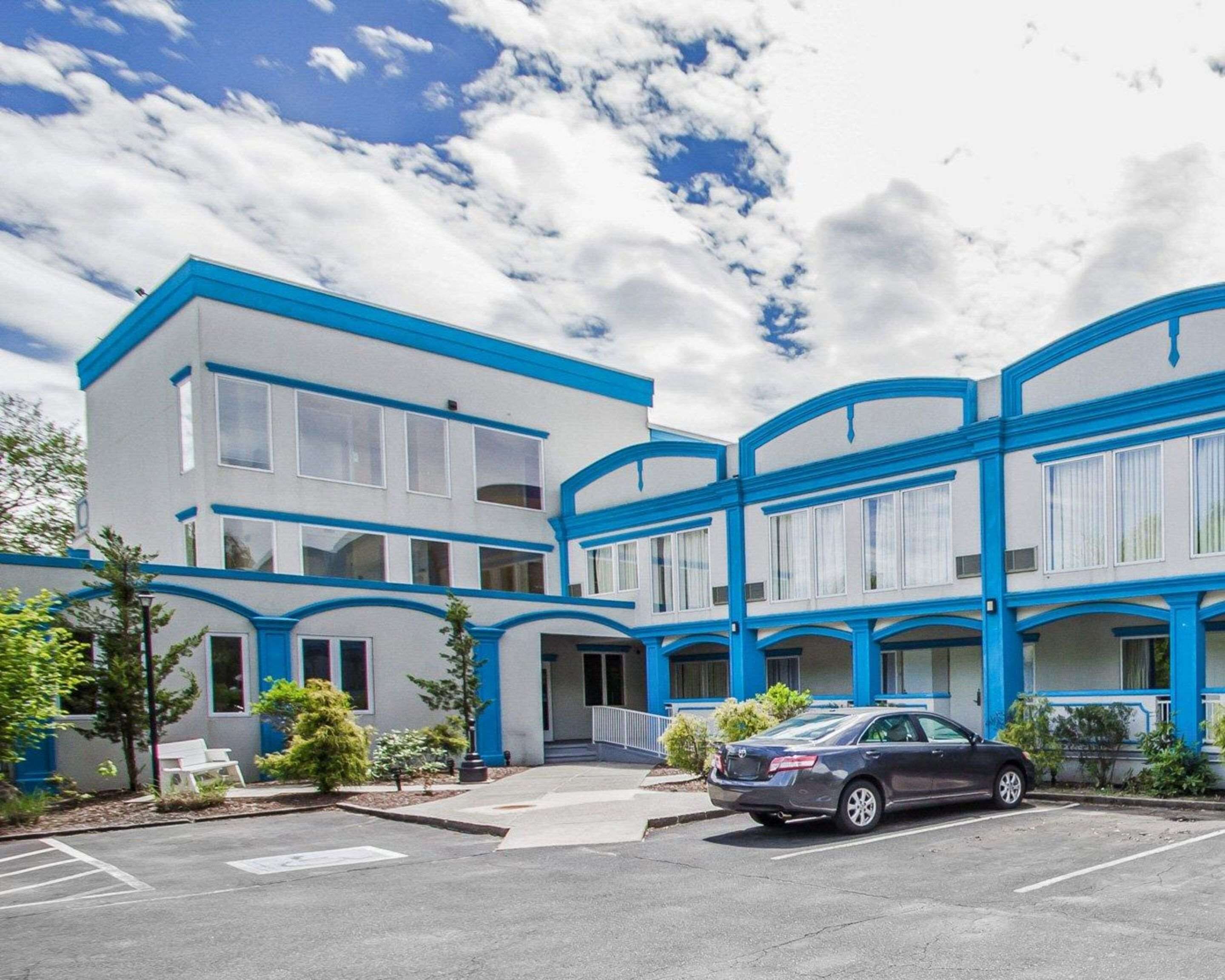 Um edifício moderno de vários andares com detalhes em azul e grandes janelas, com um estacionamento e um carro estacionado.