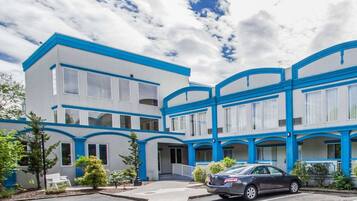 Um edifício moderno de vários andares com detalhes em azul e grandes janelas, com um estacionamento e um carro estacionado.