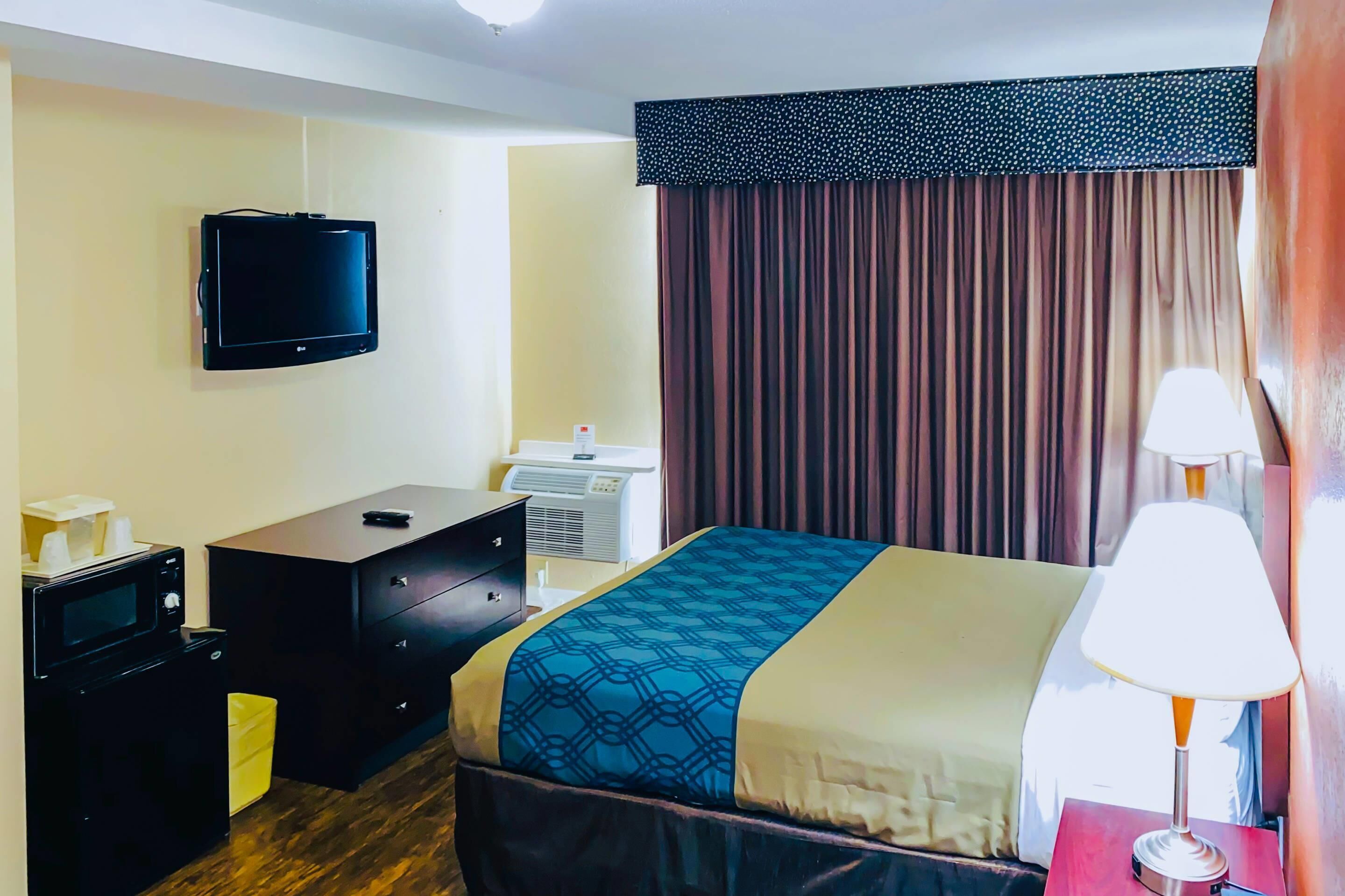 Hotelkamer met een bed, een televisie, een bureau met computer, een lamp en een raam met gordijnen.