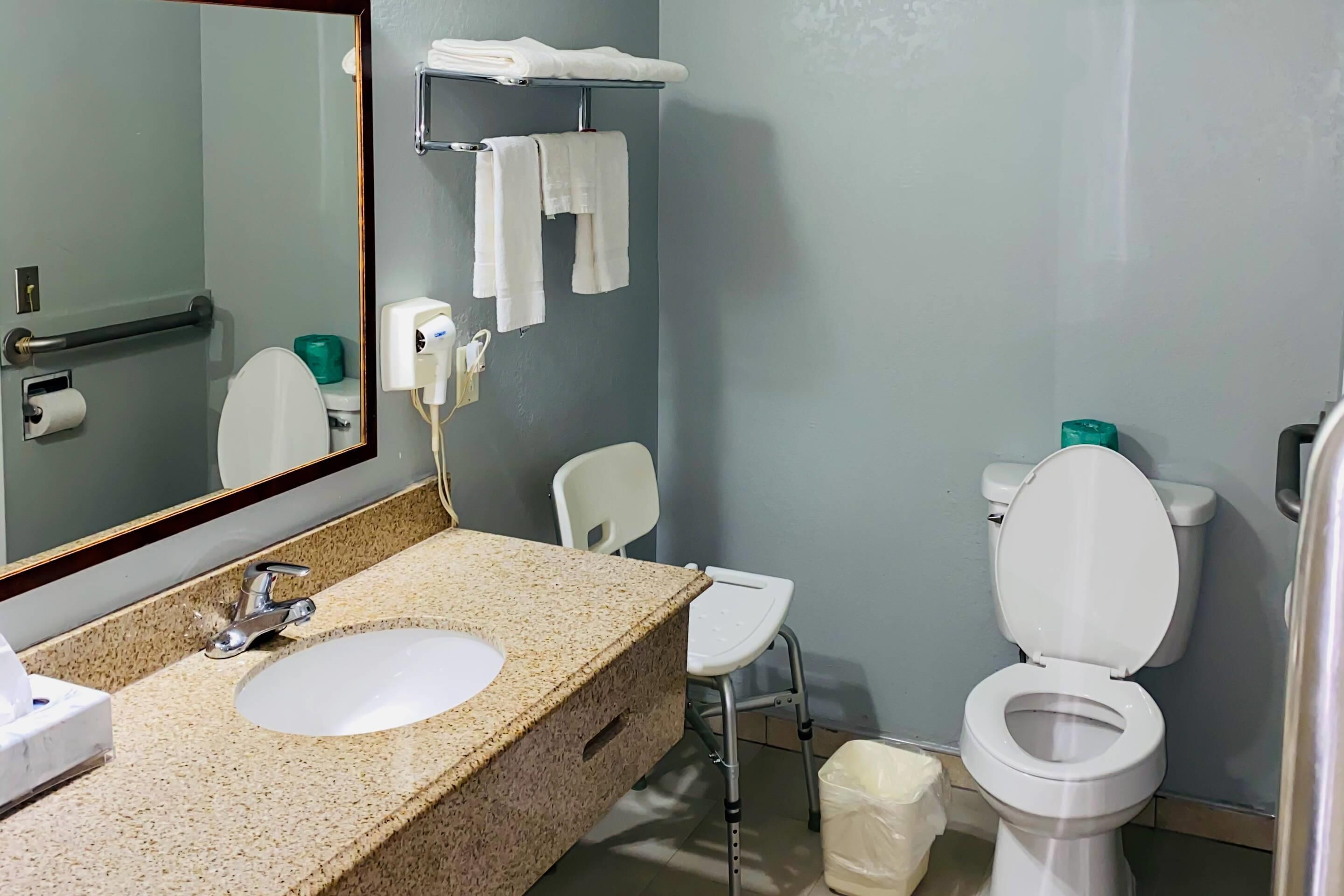 Een badkamer met een wastafel, spiegel, toilet en een stoel.