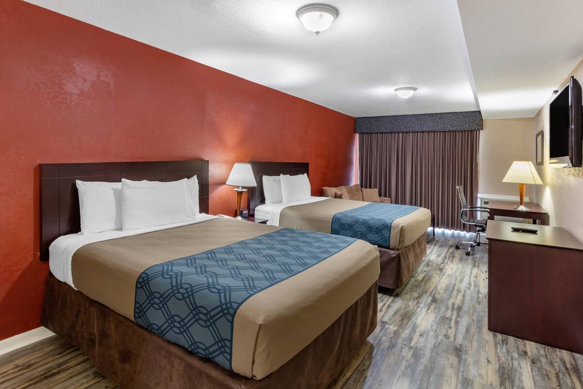 A hotel room with two beds, a desk, a chair, a TV, and a window with curtains.