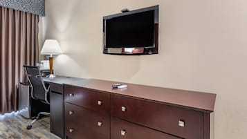 Habitación de hotel con escritorio, televisor montado en la pared, lámpara y una silla.