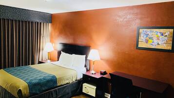 A hotel room with a bed, two bedside lamps, a desk with a chair, and a wall-mounted map.