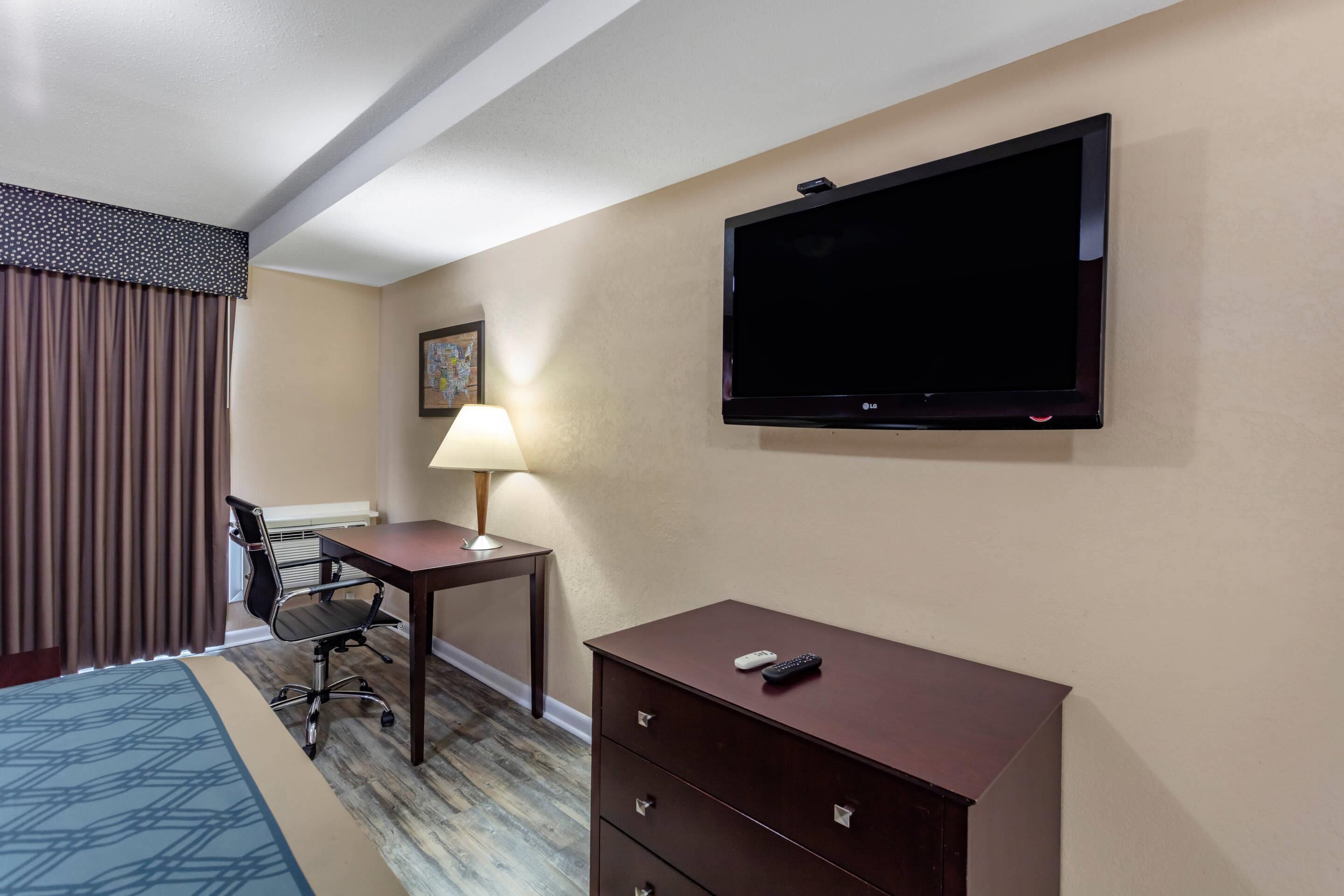 A hotel room with a bed, a desk with a lamp, a TV, and a dresser.