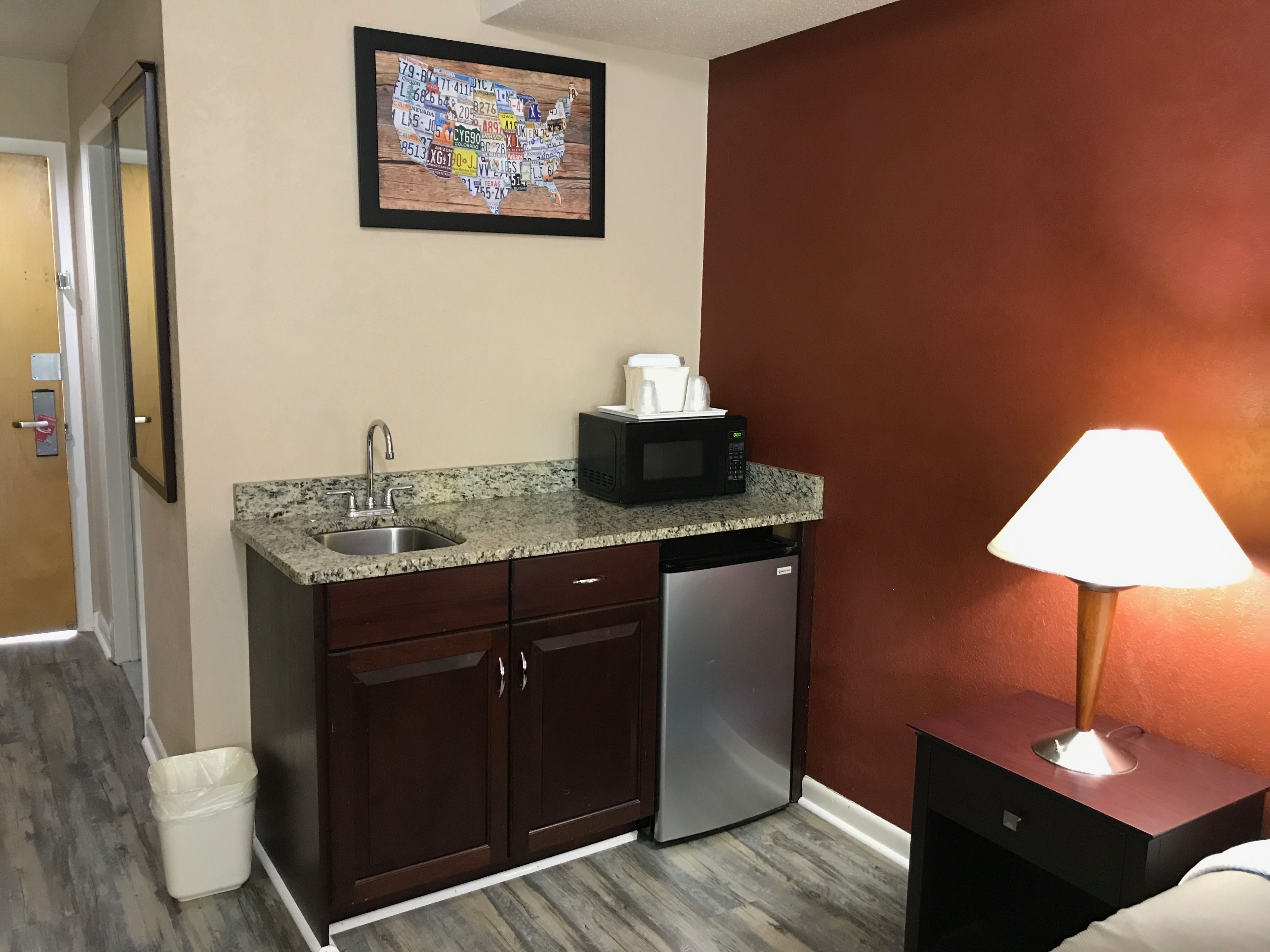 A compact hotel kitchenette with a granite countertop, stainless steel sink, and a built-in microwave.
