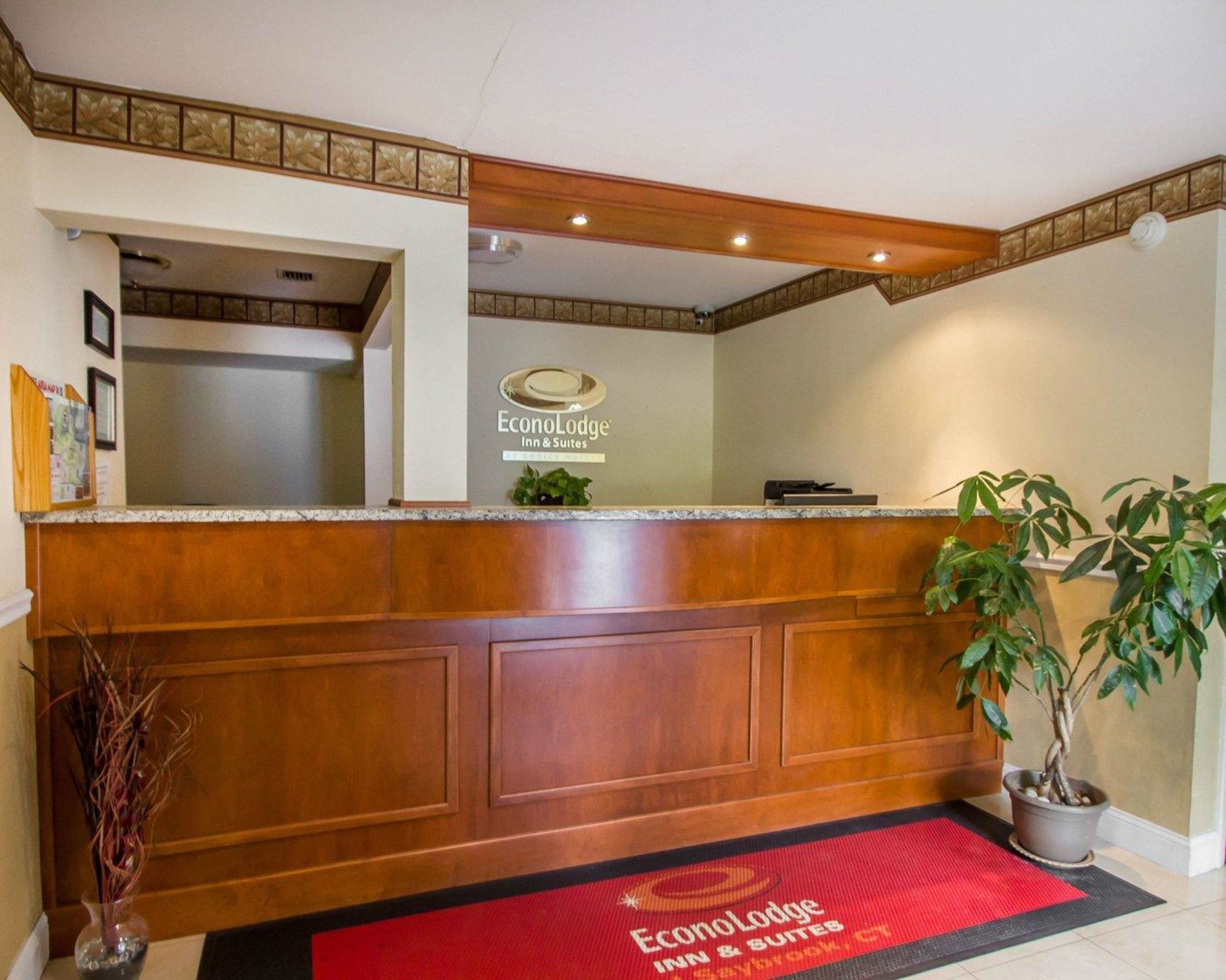 Un mostrador de recepción con detalles de madera, el logotipo de EconoLodge Inn & Suites, y una planta en maceta a la derecha.