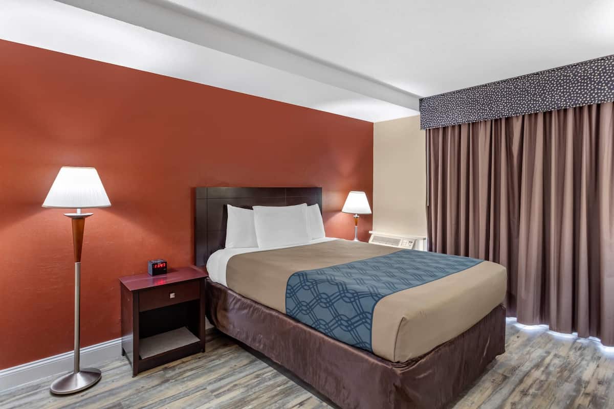 A hotel room with a bed, two bedside tables, lamps, a clock, and a window with curtains.