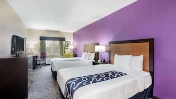 Una habitación de hotel con dos camas, un escritorio, un televisor y una ventana con cortinas.