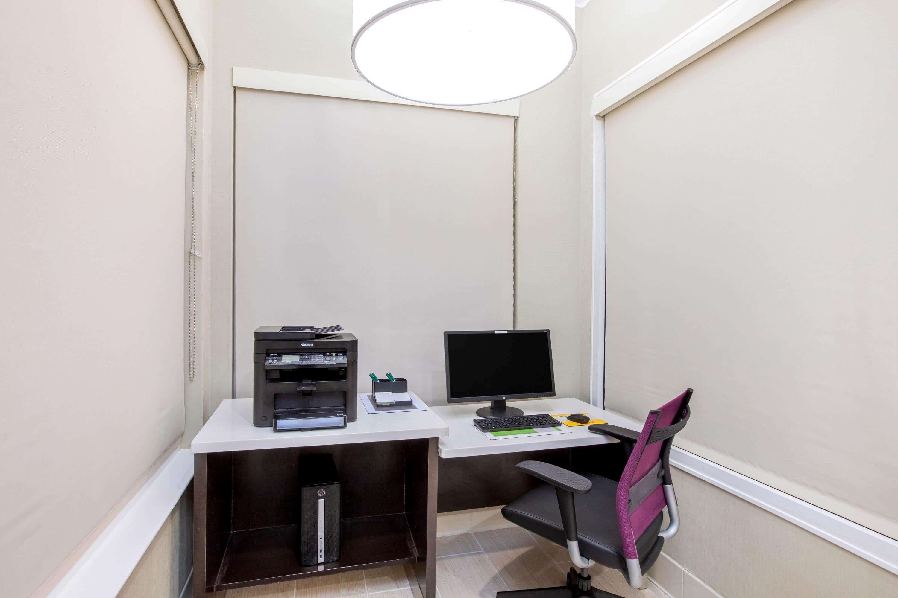 A small office space with a desk, two monitors, a printer, and a chair.