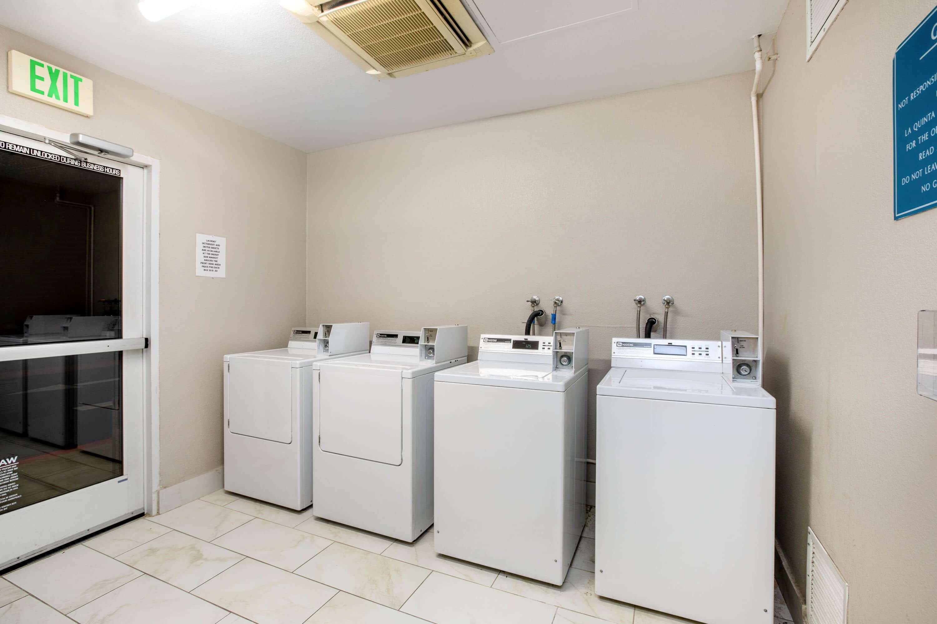 A laundry room with four washing machines, an exit sign, and a sign with instructions.