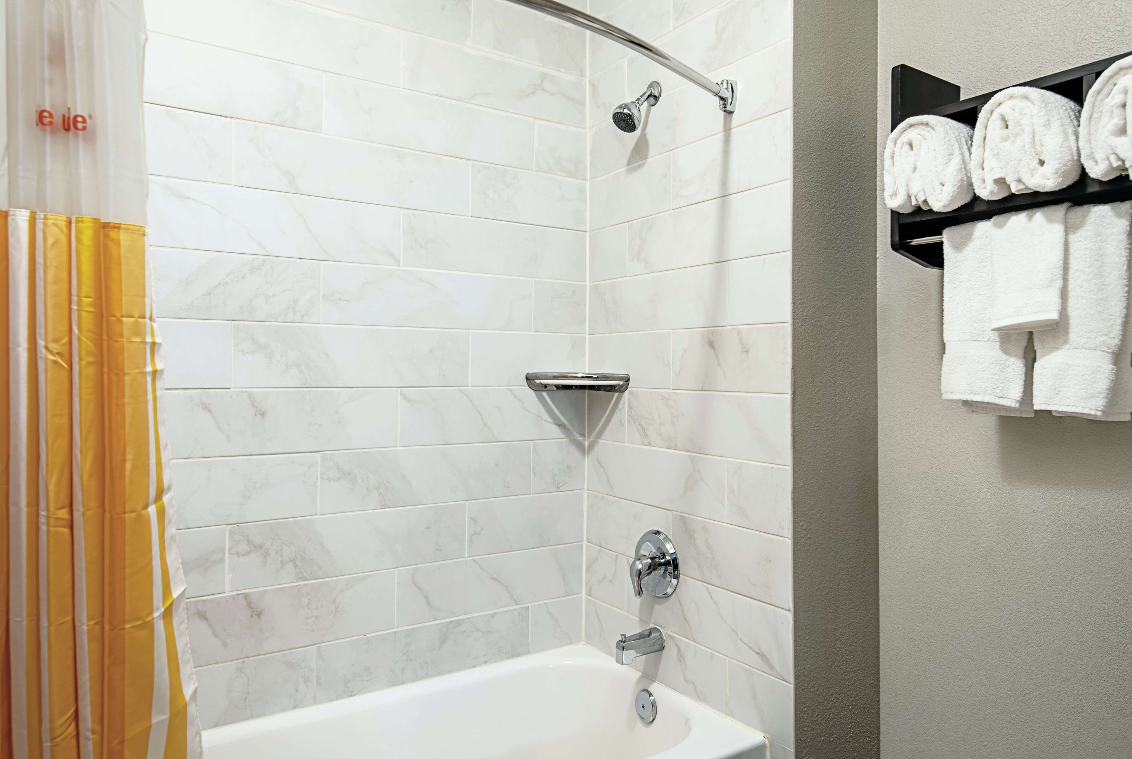 A modern bathroom with a shower, a bathtub, and a shelf with towels.