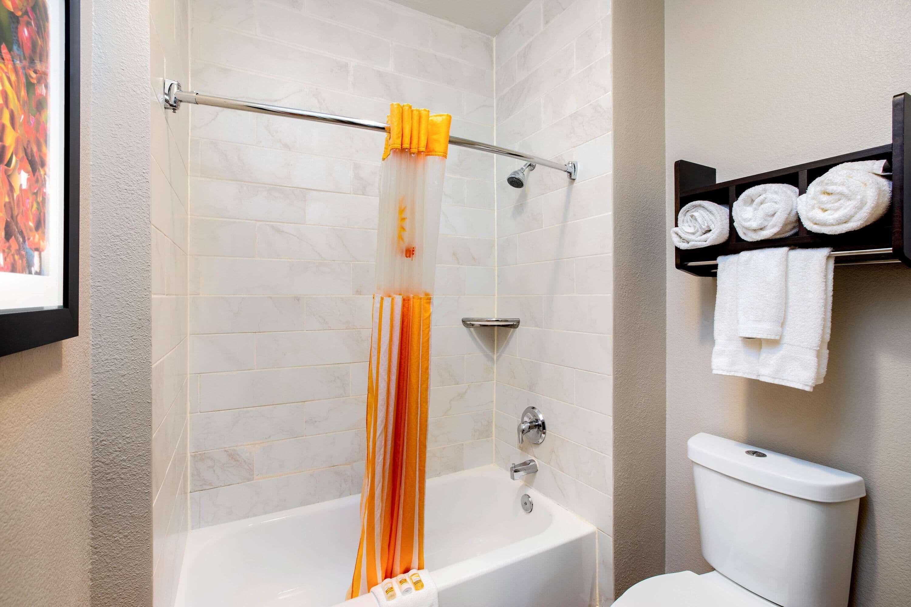 A bathroom with a bathtub, a shower curtain, a toilet, and a towel rack with towels.