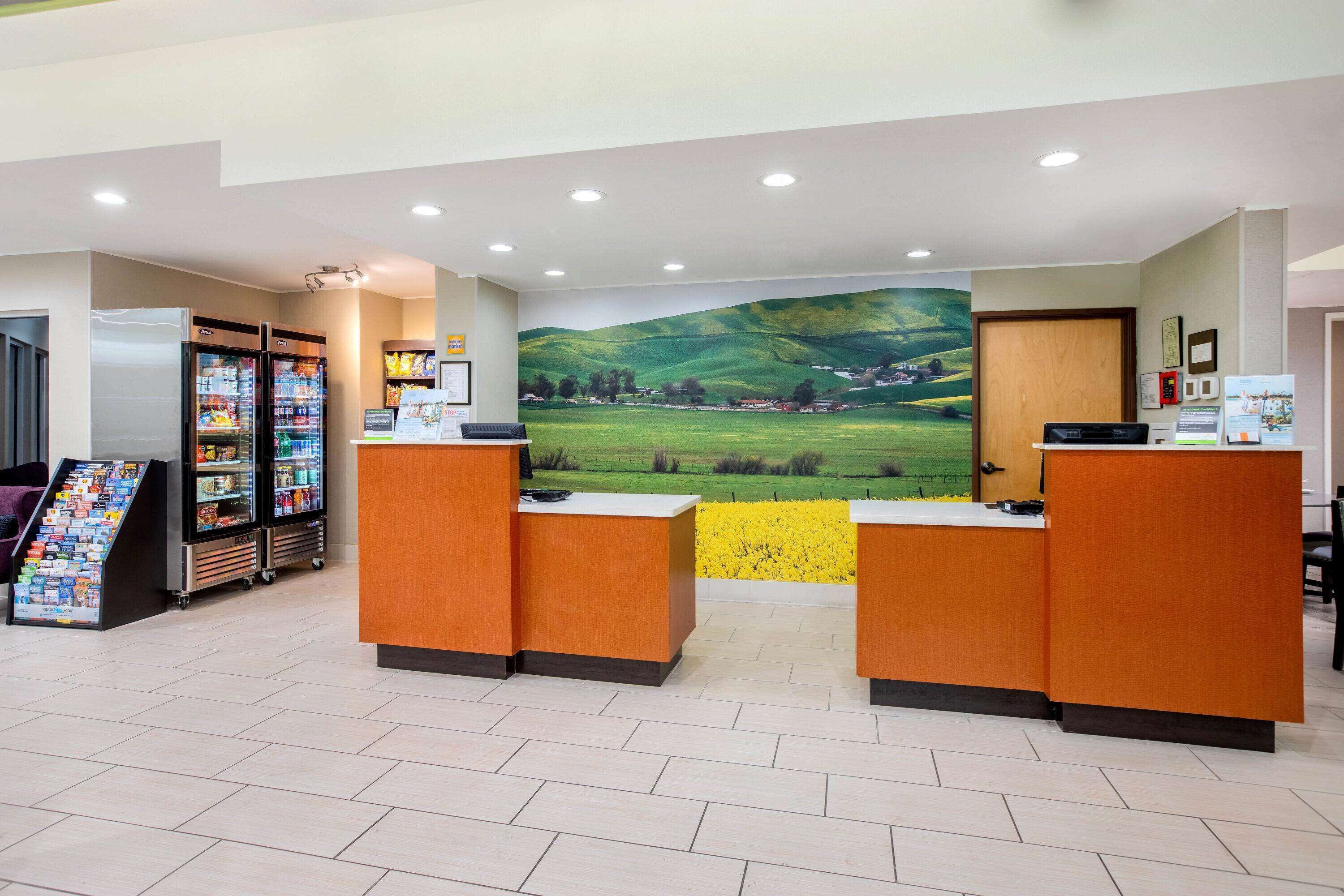 A reception area with two reception desks, a large mural of a green landscape, and a vending machine with snacks.