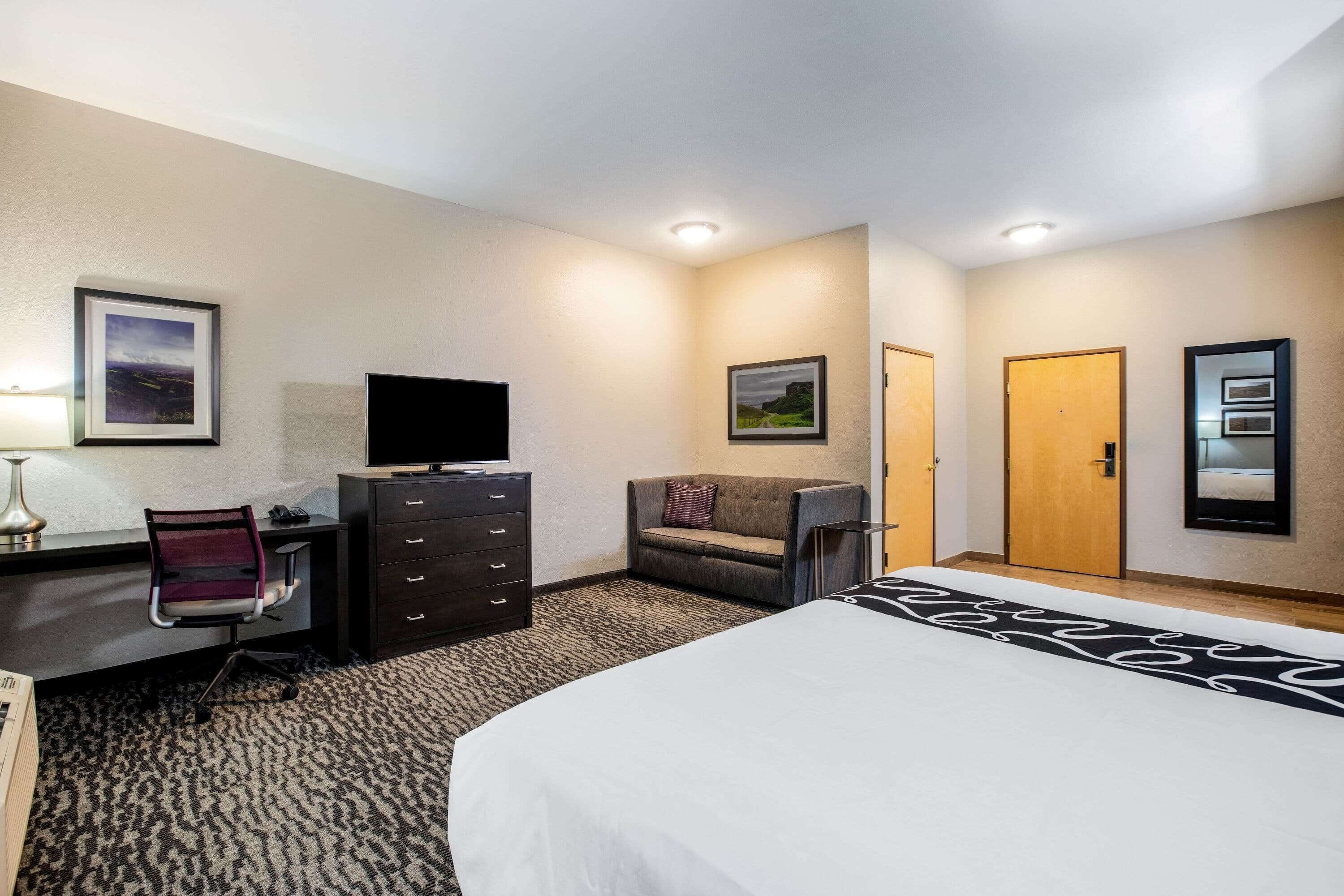 Ein Hotelzimmer mit Bett, Schreibtisch, Stuhl, Kommode, Fernseher und zwei Türen.