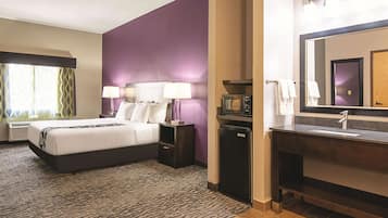 Quarto de hotel com cama, mesas de cabeceira, micro-ondas, geladeira, pia e um espelho grande.