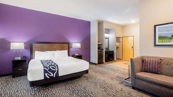 A hotel room with a large bed, two bedside tables with lamps, a sofa, and a bathroom visible through an open door.