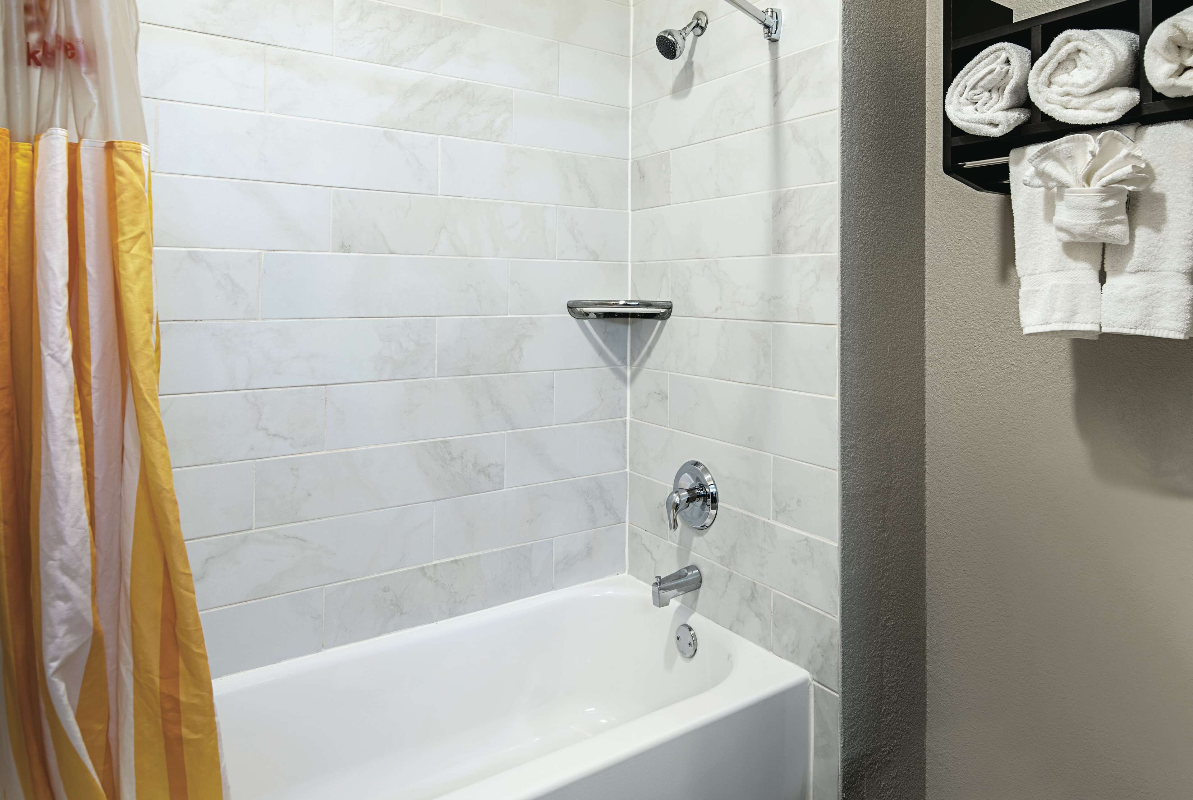 A bathroom with a white bathtub, a showerhead, and a towel rack with towels.