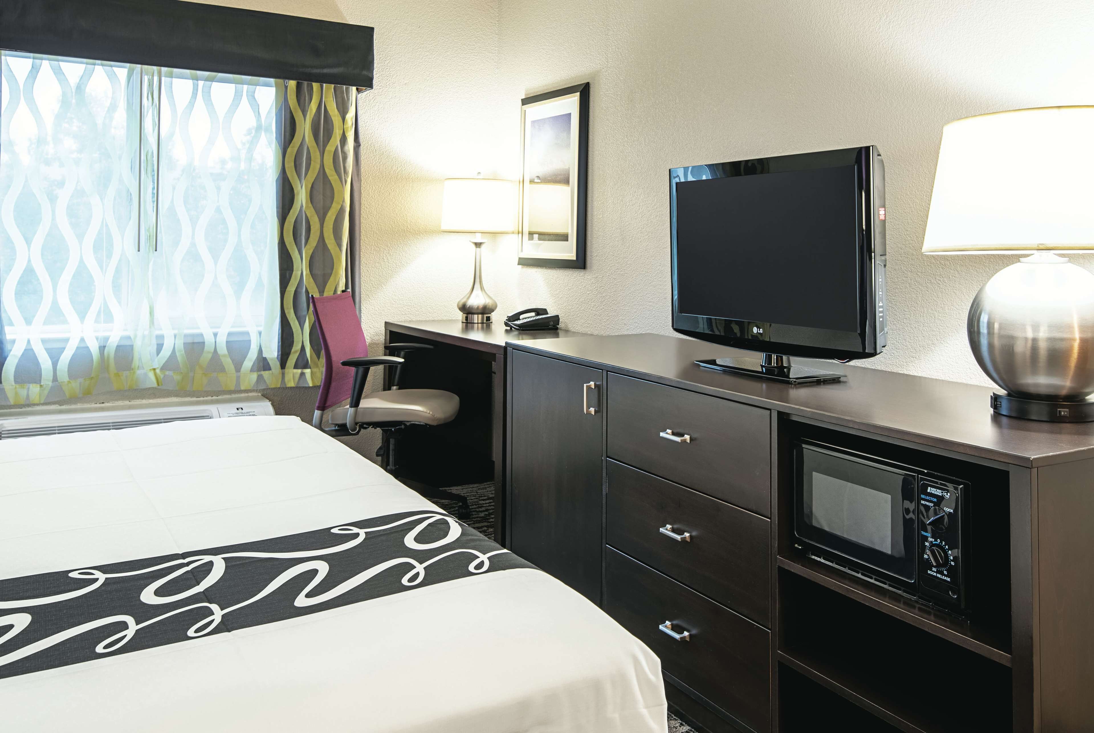 Hotelkamer met een bed, een bureau met een televisie, een lamp, een telefoon en een magnetron.