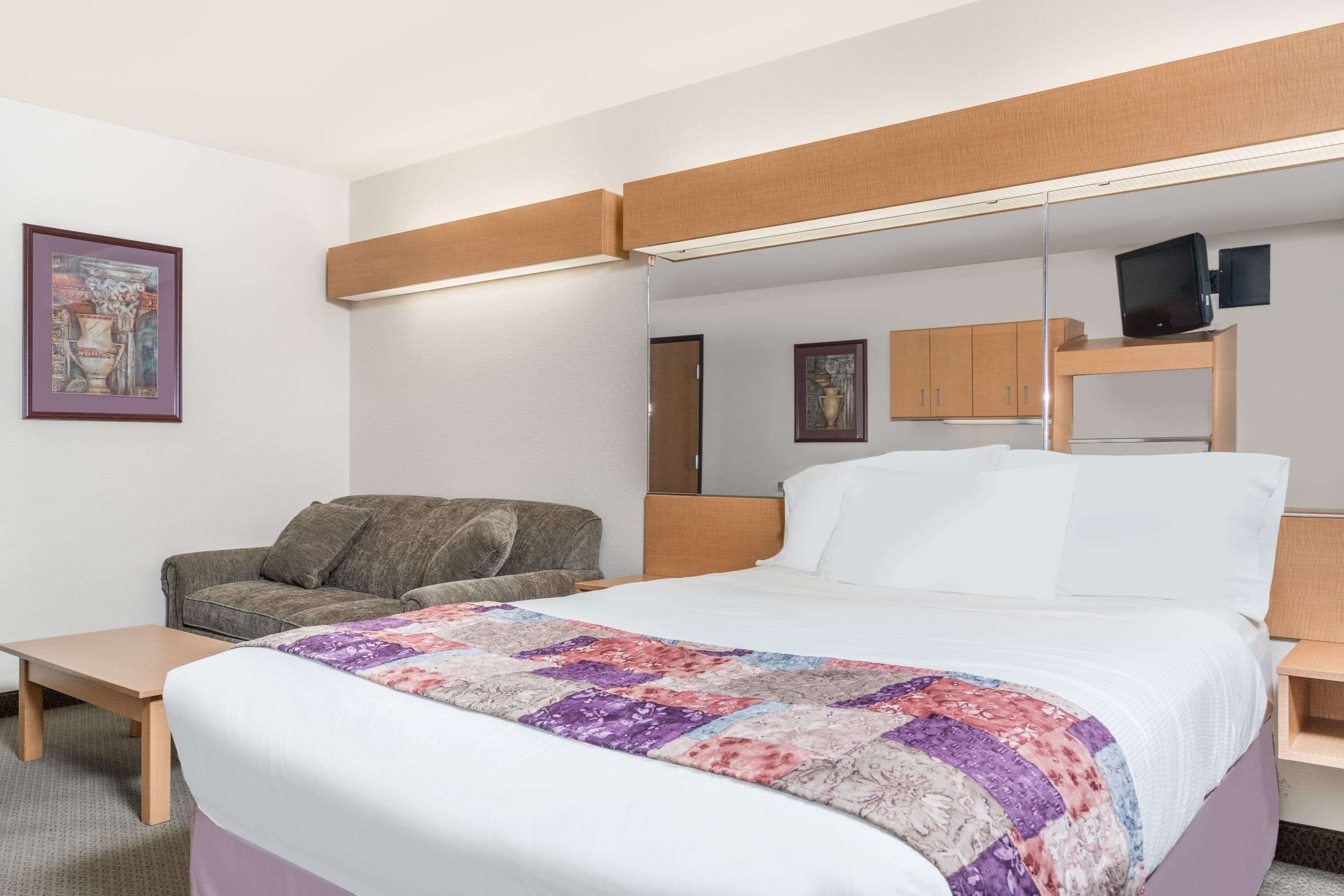 A hotel room with a bed, a chair, a small table, a mirror, and a television on a shelf.