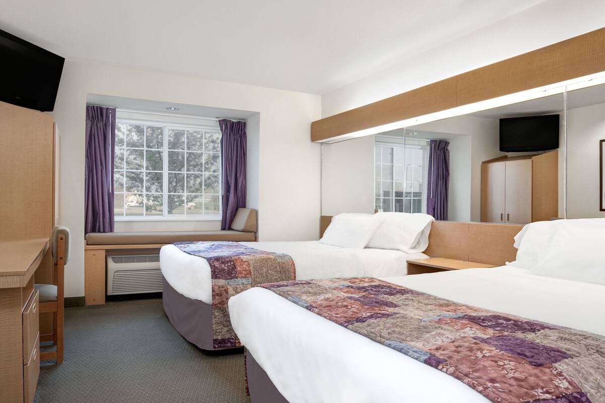 A hotel room with two beds, a desk, a chair, a window with curtains, a television, and a wardrobe.