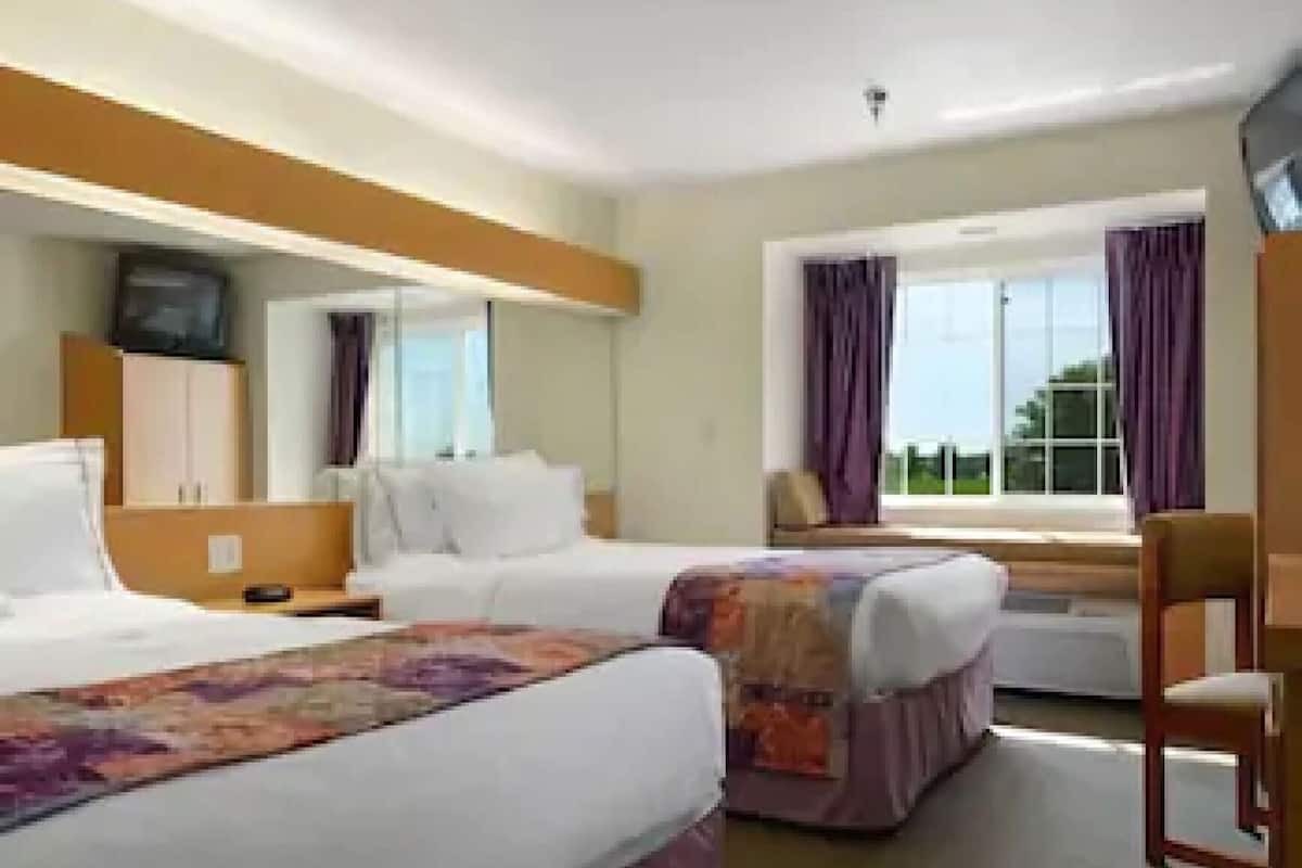 A hotel room with two beds, a television, a window with curtains, and a view of the outdoors.