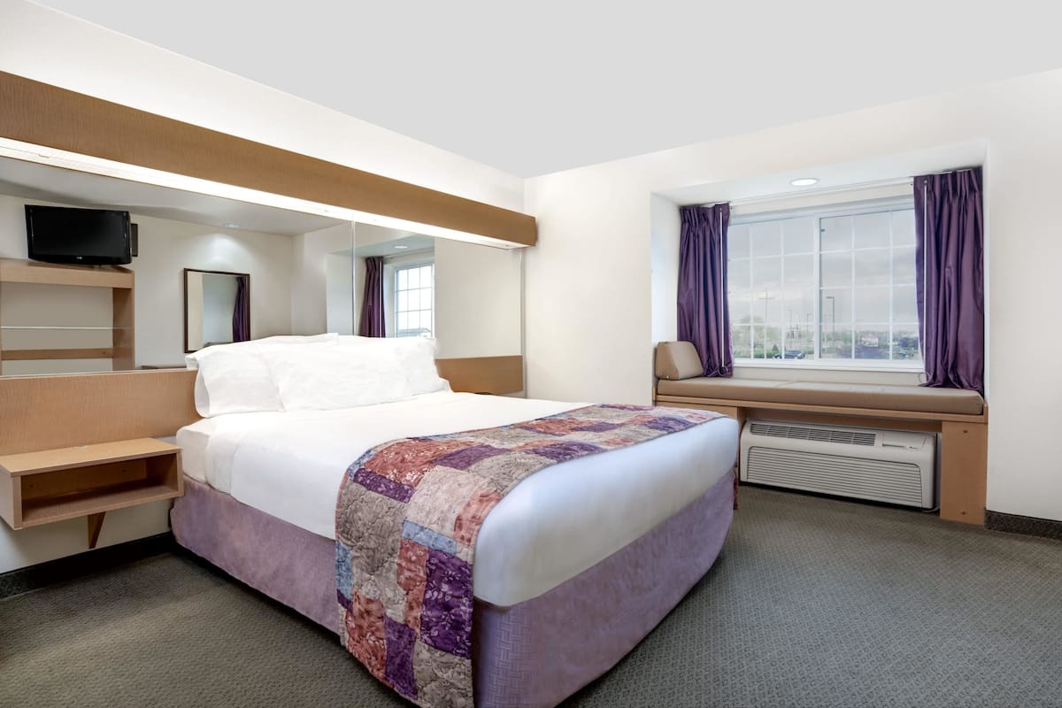 A hotel room with a bed, a TV, a window with curtains, and a built-in bench.